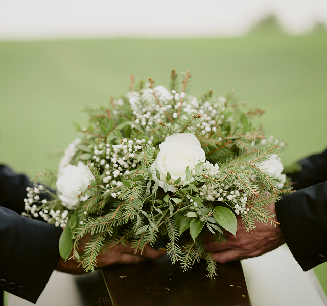 funeral directors holding a flower arrangement